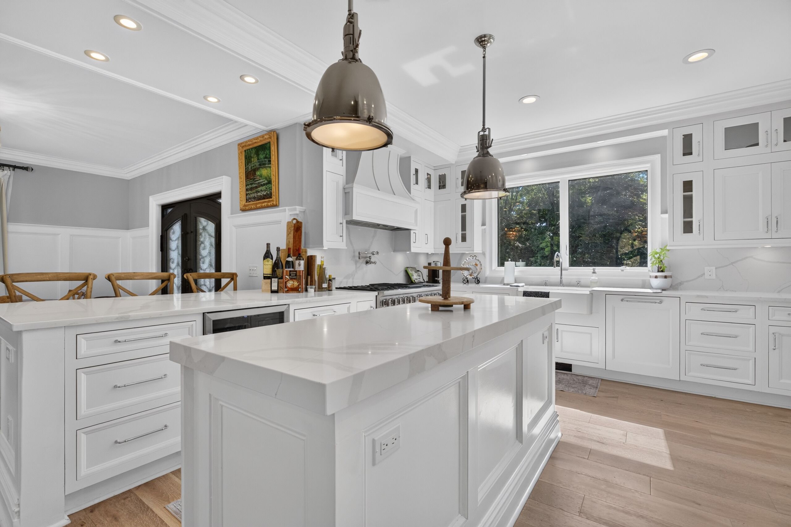 A modern kitchen with white cabinetry, a large island, pendant lighting, and a view of the outdoors through a window.