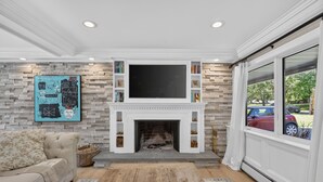 A living room with a fireplace, a sofa, a coffee table, and a bookshelf. - Luxury Home w/ Secret Room & Royal Master Suite (Wyckoff)