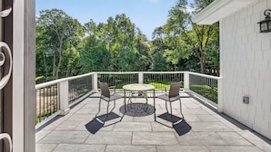 A covered patio with a round table and chairs, surrounded by a white railing, overlooking a lush green landscape. - Luxury Home w/ Secret Room & Royal Master Suite (Wyckoff)