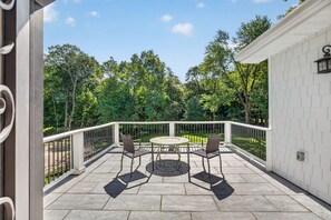 Eira coberta com mesa redonda e cadeiras, rodeada por um guarda-corpo branco, com vista para uma paisagem verde exuberante.