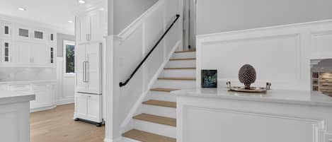 A modern kitchen with white cabinetry, a wooden staircase, and a countertop with decorative items.