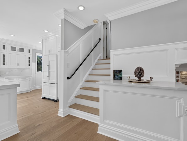 A modern kitchen with white cabinetry, a wooden staircase, and a countertop with decorative items.