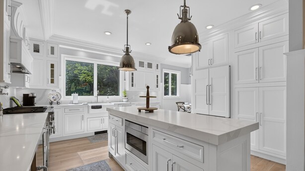 A modern kitchen with white cabinetry, a central island, stainless steel appliances, pendant lighting, and large windows. - Luxury Home w/ Secret Room & Royal Master Suite (Wyckoff)