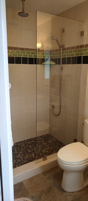 Eine begehbare, gläserne Dusche mit Handbrause, Toilette und ein Boden mit Kieselmuster.