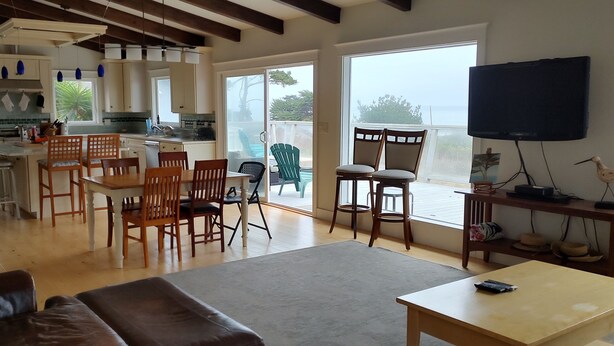A spacious living area with a sofa, dining table, and chairs, a kitchen with modern appliances, and a large window offering a view. - Beach house in quaint Half Moon Bay with unimpeded view and beach access (Half Moon Bay)