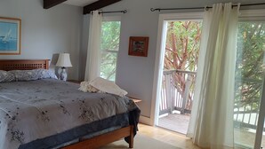 A bedroom with a bed, a nightstand, a lamp, a window with curtains, and a painting on the wall. - Beach house in quaint Half Moon Bay with unimpeded view and beach access (Half Moon Bay)