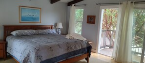 Ein Schlafzimmer mit einem Bett, einem Nachttisch, einer Lampe, einem Fenster mit Vorhängen und einem Bild an der Wand.