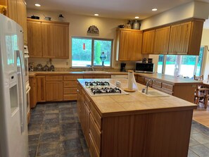 A kitchen with wooden cabinets, a gas stove, a sink, and a window with a view of greenery. - Private Retreat with Stunning Views (Acme)