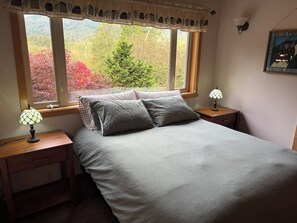 A bedroom with a bed, two bedside tables, a window with a view of trees, and a wall-mounted lamp. - Private Retreat with Stunning Views (Acme)