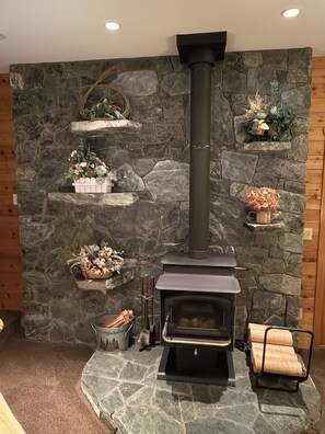 A stone fireplace with a black chimney, surrounded by decorative shelves with plants and a cozy seating area. - Private Retreat with Stunning Views (Acme)