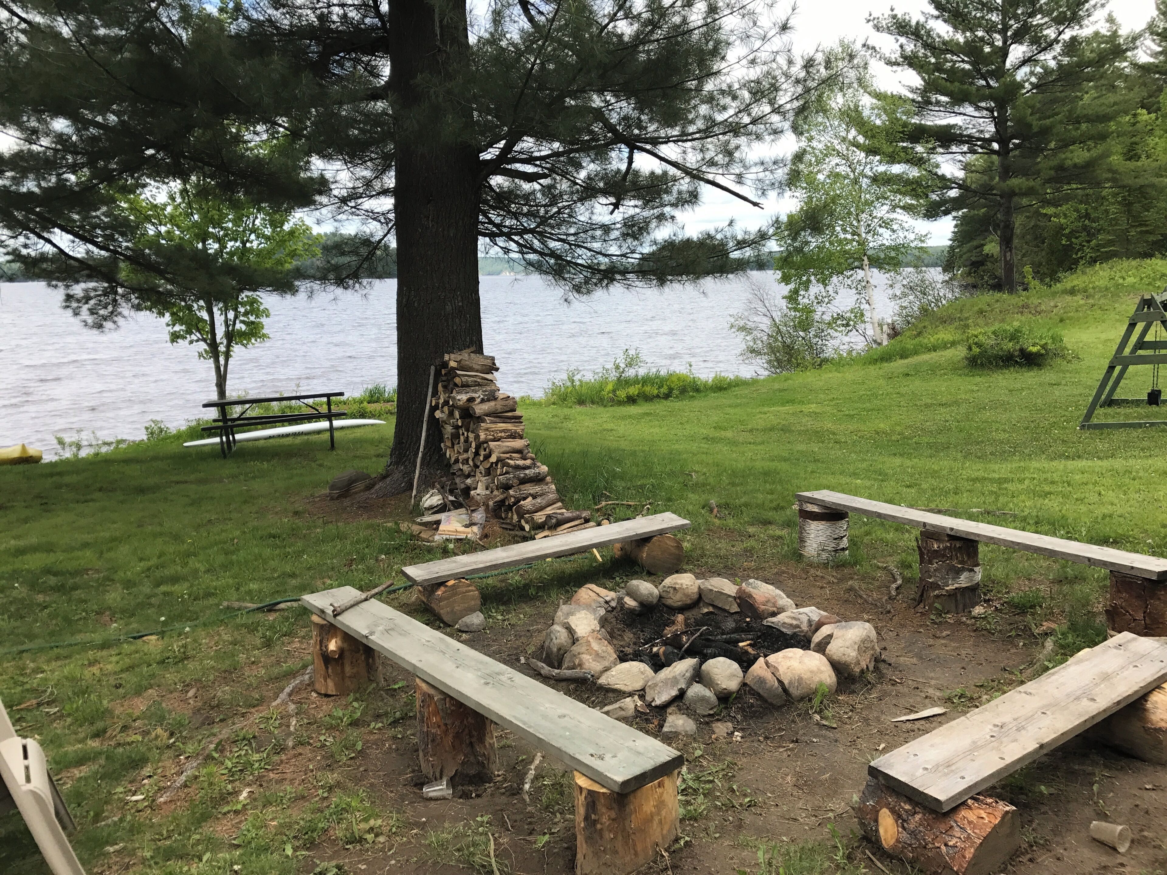 A lakeside campsite with a fire pit, picnic table, and benches.