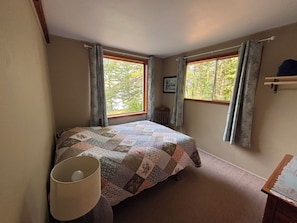 Une chambre à coucher avec un lit, une table de chevet, une lampe et deux fenêtres avec des rideaux.