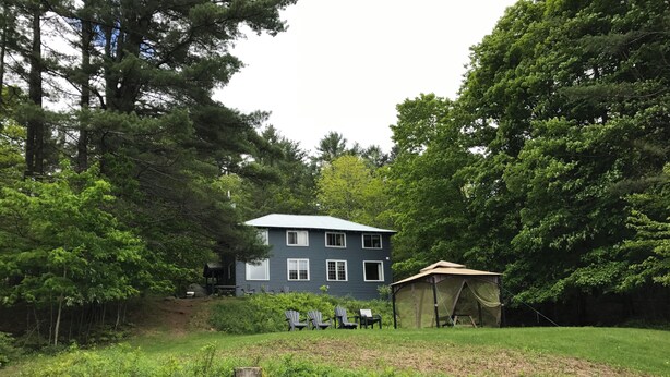 A two-story house with a fenced yard, surrounded by dense trees. - The “Lower Dancehall”: A lakeview forested cottage (Port Sydney)