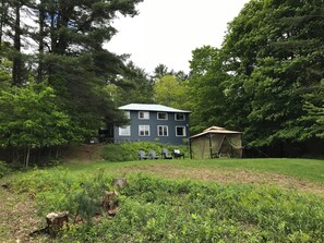 A two-story house with a fenced yard, surrounded by dense trees. - The “Lower Dancehall”: A lakeview forested cottage (Port Sydney)