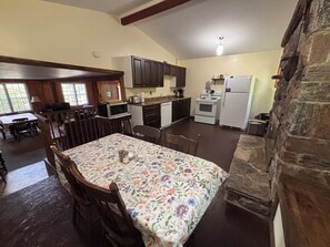 Un coin repas avec une nappe à motifs floraux, des chaises en bois et une vue sur la cuisine et ses appareils.