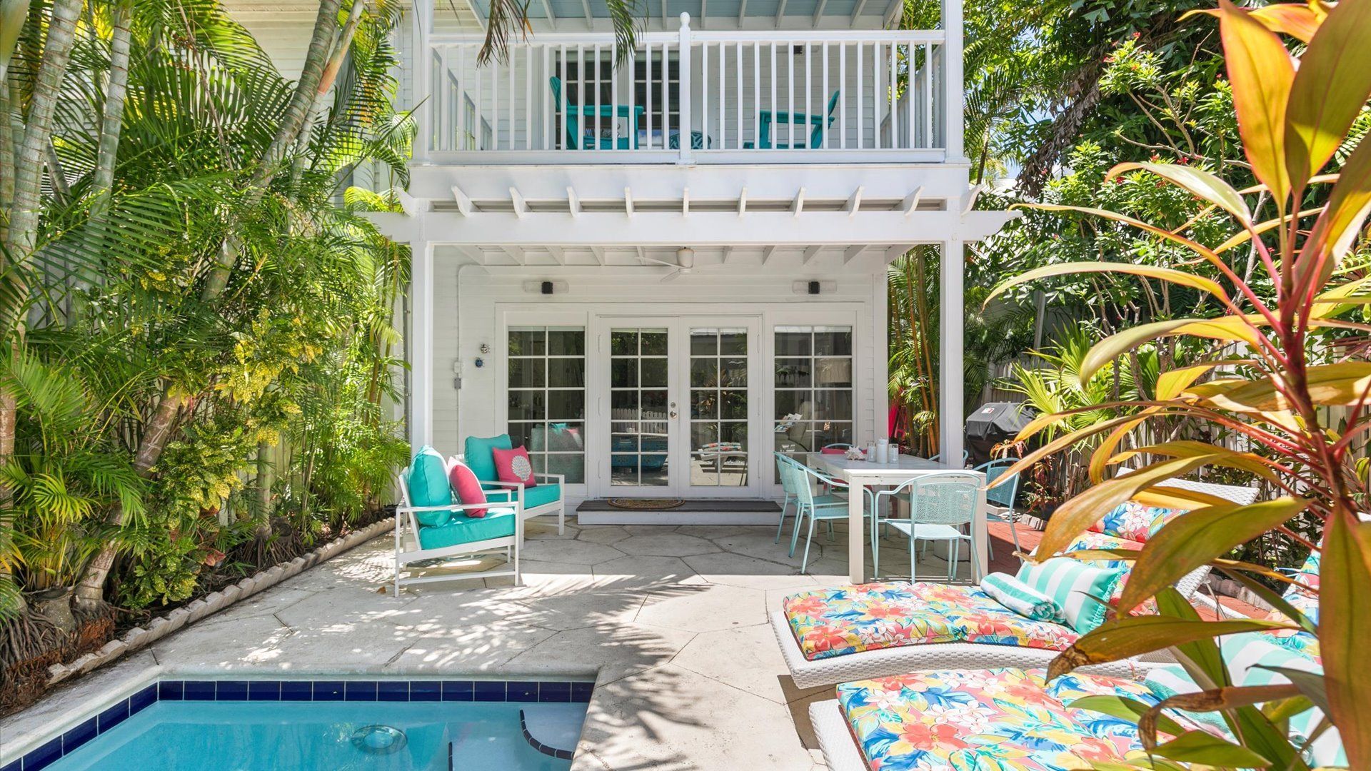 A two-story house with a balcony, a pool, and outdoor furniture.
