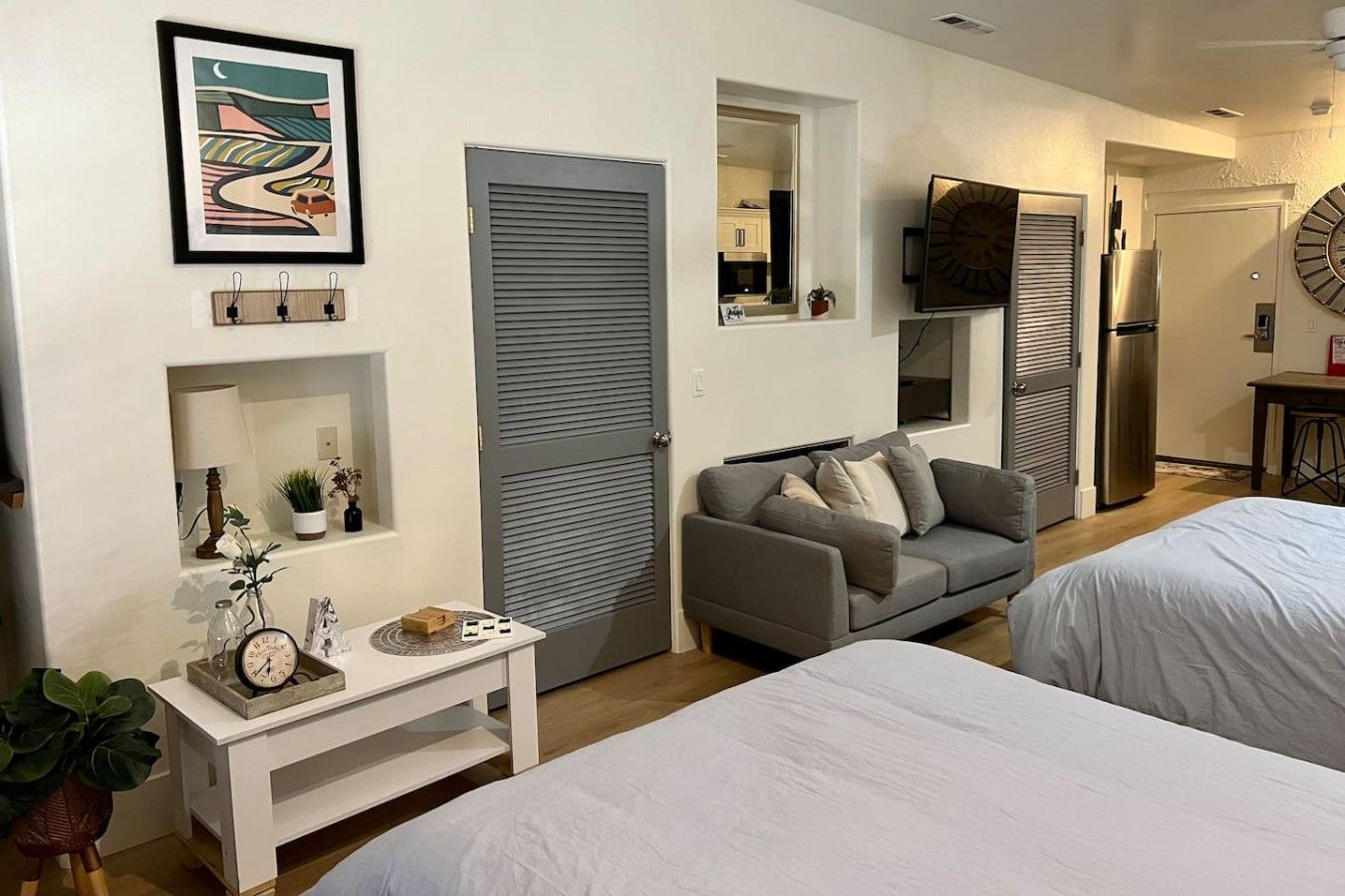 Quarto moderno com duas camas, um sofá cinza, uma mesinha com um relógio e um quadro na parede.