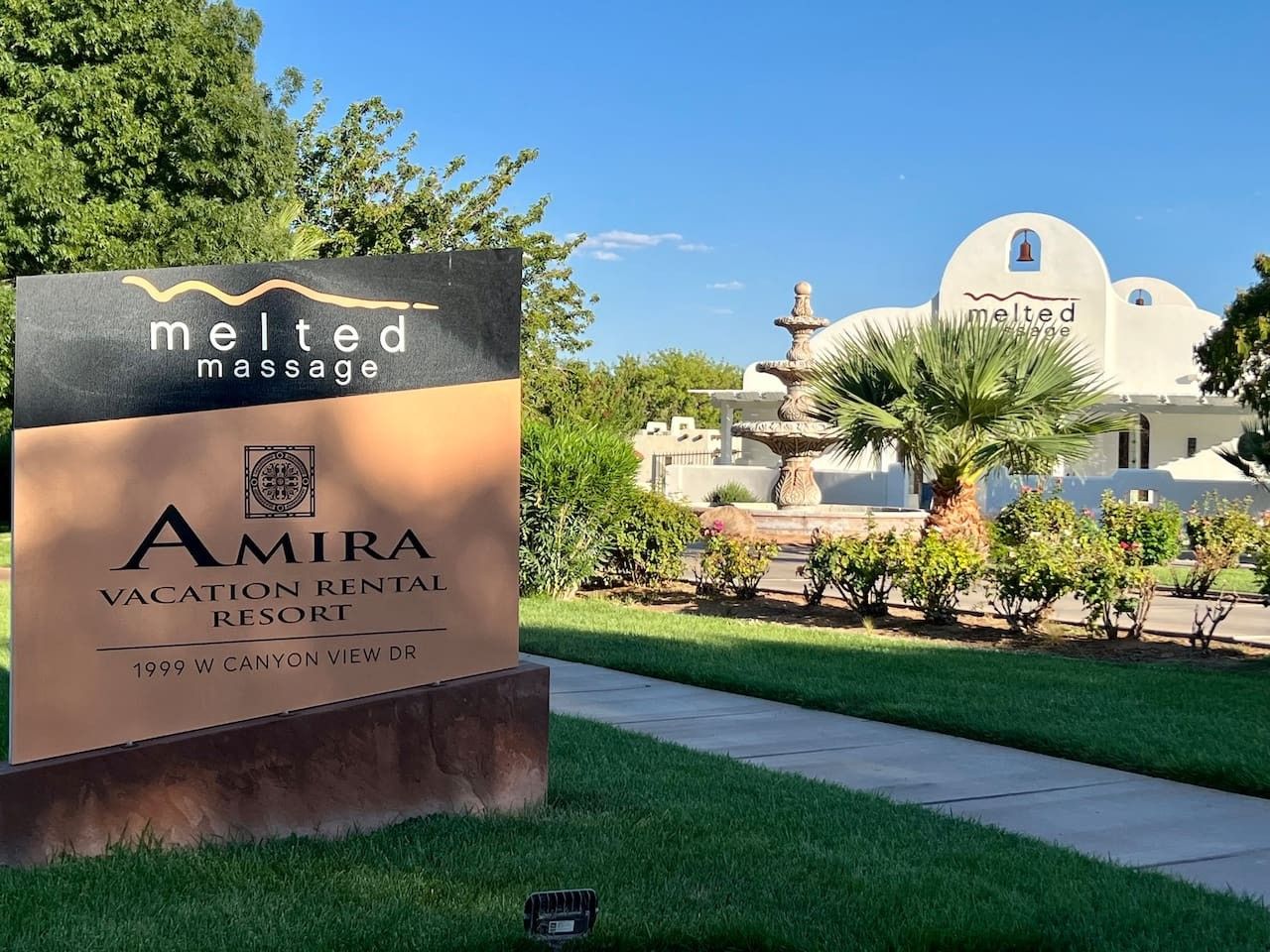 Placa para Amira Vacation Rental Resort com logotipo de massagem 'derretido', uma fonte e um edifício branco com cúpula.