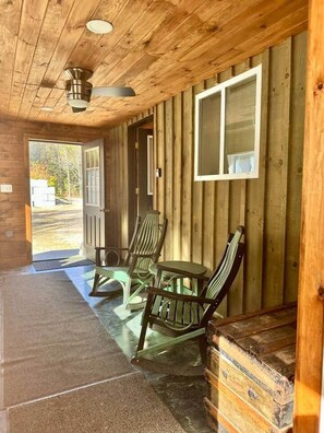 A wooden cabin with a porch, rocking chairs, and a table. - Green Stone Getaway, cozy cabin close to Killington! (Bethel)