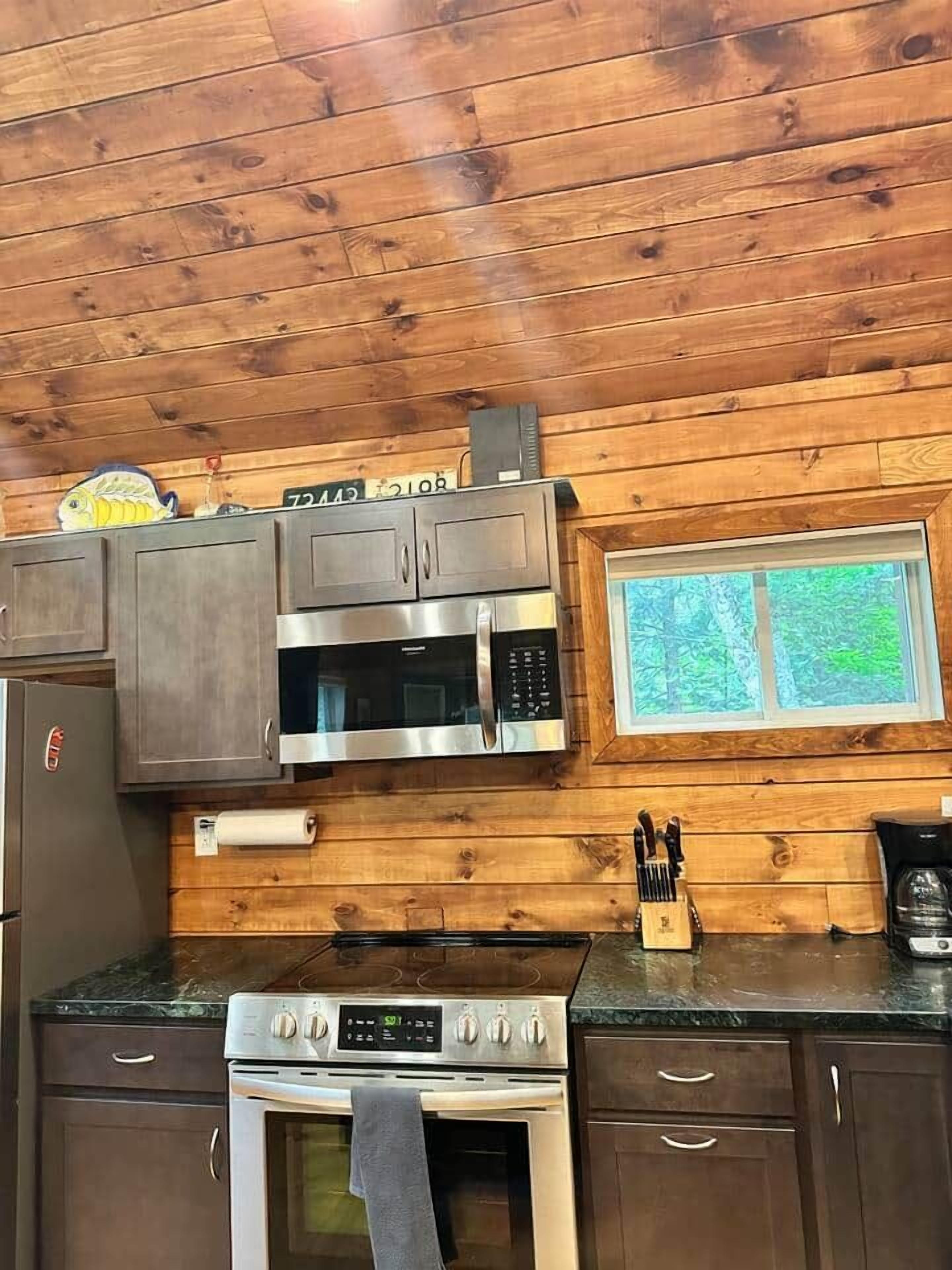 A kitchen with wooden walls, a window, and stainless steel appliances including a microwave and oven.