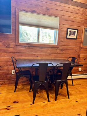 A wooden interior with a table and chairs, a window with a view, and a power outlet. - Green Stone Getaway, cozy cabin close to Killington! (Bethel)