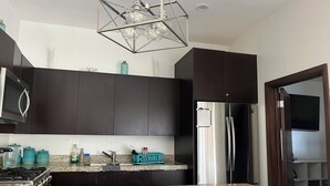 Una cocina moderna con armarios oscuros, un refrigerador de acero inoxidable, una encimera de granito y una lámpara colgante de diseño geométrico.