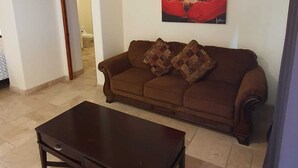 Een woonkamer met een bruine bank, een donkerhouten salontafel en een schilderij van een rode bloem aan de muur.