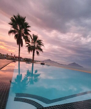 A swimming pool with clear water reflecting palm trees and a sunset sky.