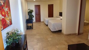 Een hotelkamer met een bed, een bureau, een stoel, een potplant en een schilderij aan de muur.