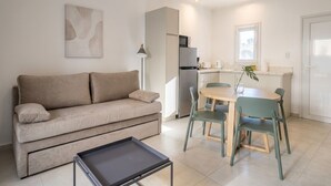 A modern living room with a sofa, a dining table with chairs, a small coffee table, and a kitchen area with a refrigerator and a microwave. - Apartment for 4 with a separate bedroom (Azul)