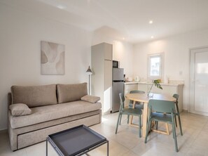 Un salon moderne comprenant un canapé, une table à manger avec des chaises, une petite table basse et un coin cuisine avec un réfrigérateur et un four à micro-ondes.