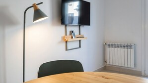A room with a round wooden table, a black chair, a wall-mounted TV, a floor lamp, and a radiator. - Apartment for 4 with a separate bedroom (Azul)