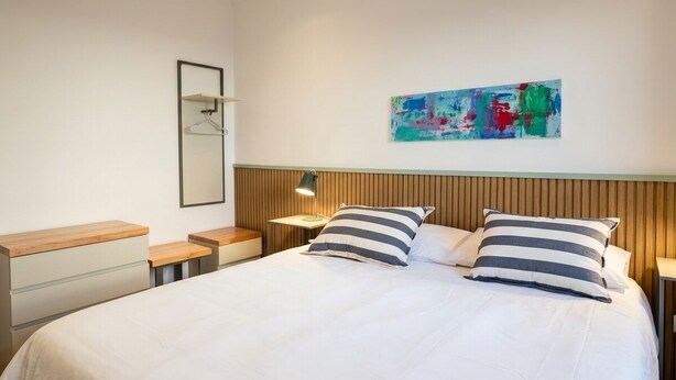 A hotel room with a large bed, bedside tables, a hanging light, a wall-mounted artwork, and a wooden headboard. - Apartment for 4 with a separate bedroom (Azul)