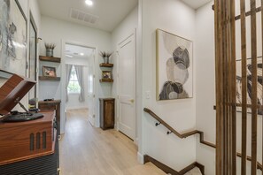 A hallway with a wooden piano, a staircase with a handrail, and a framed abstract painting on the wall.