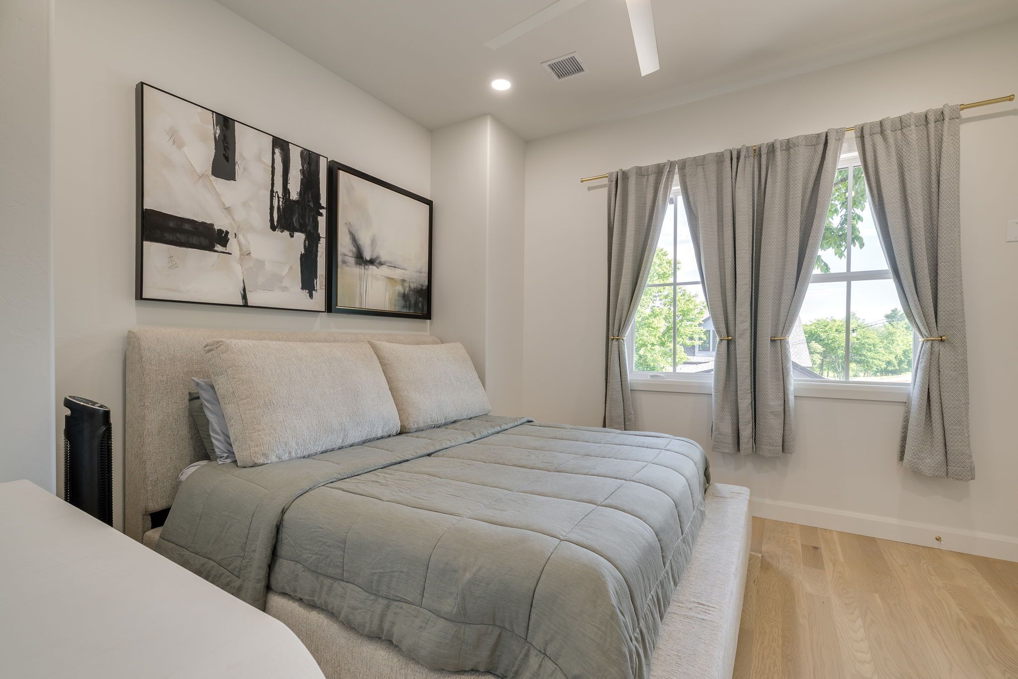 Un dormitorio con cama, dos cuadros abstractos, una ventana con cortinas y un radiador.