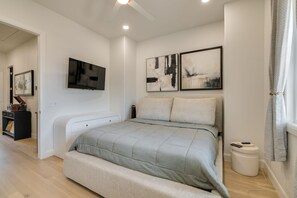 Un dormitorio moderno con una cama, un televisor y obras de arte en la pared.