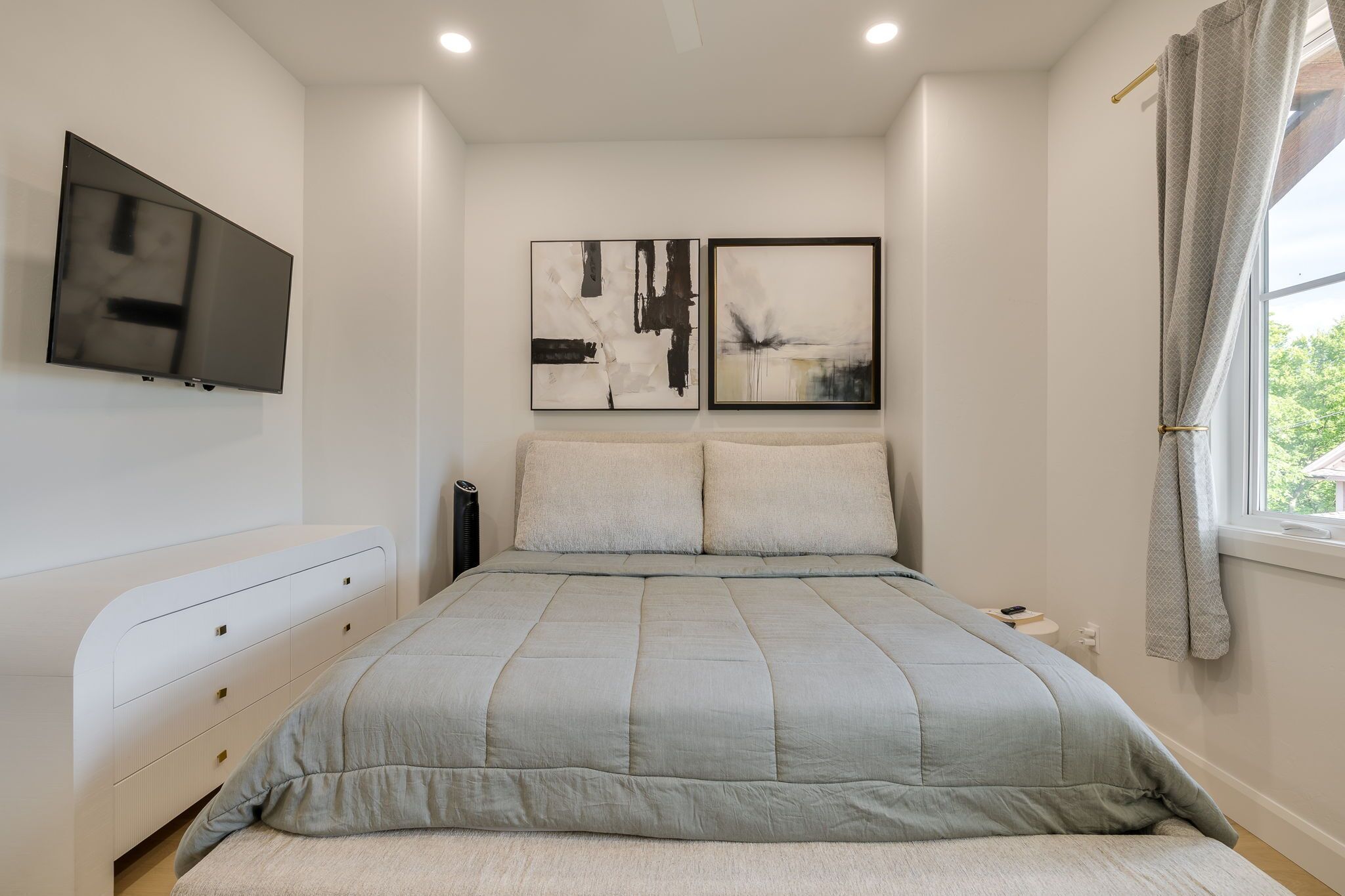 A bedroom with a bed, a TV mounted on the wall, and two abstract paintings.