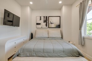 A bedroom with a bed, a TV mounted on the wall, and two abstract paintings.