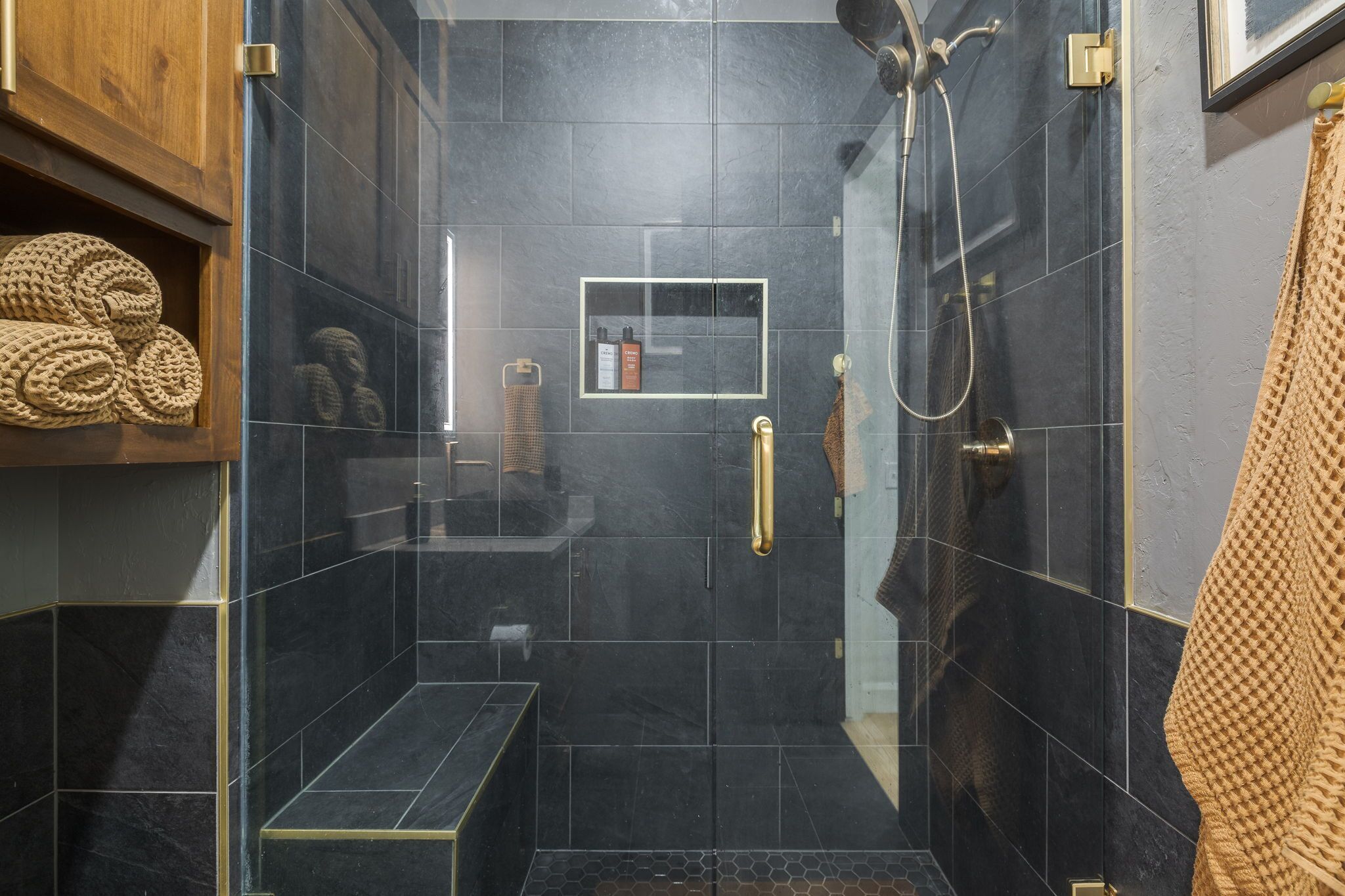 A modern bathroom with a glass shower enclosure, a bench, and a towel rack.