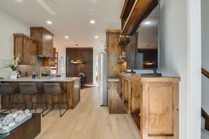 Una cocina moderna con armarios de madera, una isla central con taburetes de bar y un televisor de pantalla plana grande montado en la pared.