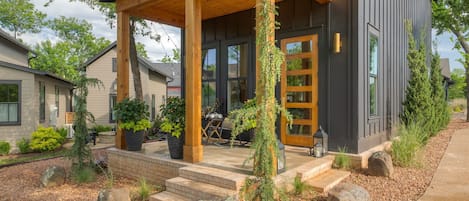 A modern house with a wooden porch, large windows, and a stone pathway leading to the entrance.
