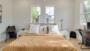 Quarto com cama, duas janelas, escrivaninha, cadeira e ventilador de teto.