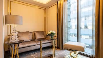 A modern hotel room with a sofa, a side table, a lamp, and a view of a building through large windows.