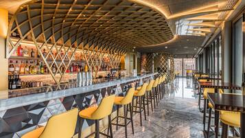 A bar area with a curved ceiling, a long counter with bottles, and yellow bar stools.