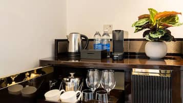 A hotel room's minibar with a coffee maker, water bottles, and a potted plant.