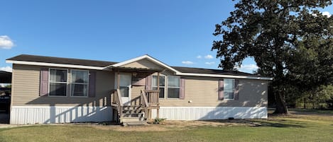 Une maison mobile de plain-pied, dotée d’un porche à l’avant, d’un petit escalier et d’un drapeau.