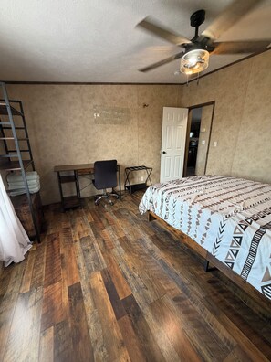 A bedroom with a bed, a desk, a chair, a ladder, and a ceiling fan.