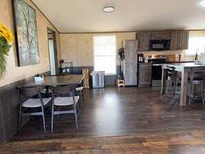 A modern kitchen with wooden cabinets, a dining area with chairs, and a large window providing natural light.