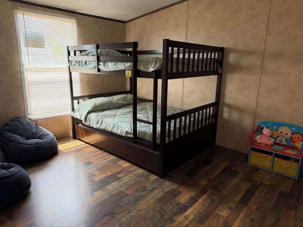 Dans une chambre avec un parquet en bois, on trouve un lit superposé, un fauteuil en forme de poire et un espace de jeux pour enfants avec des jouets.