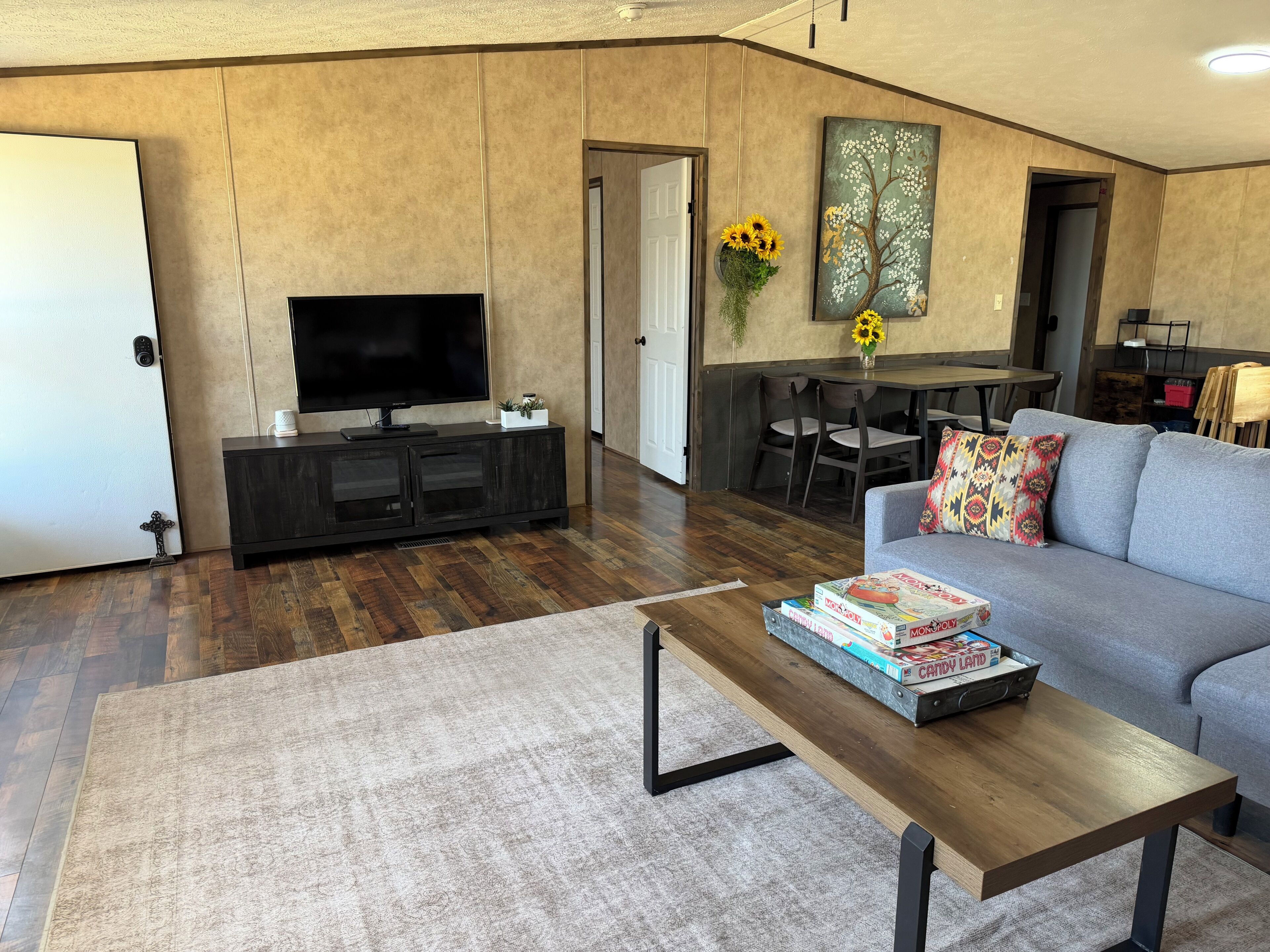 A living room with a flat-screen TV, a sofa, a coffee table, and a dining area with chairs.